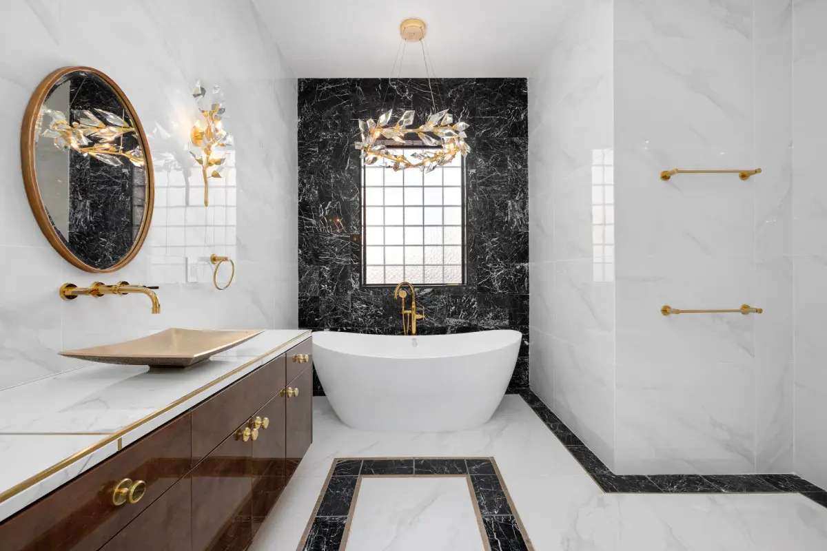 A bathroom with marble walls and floors, a tub, sink and mirror.